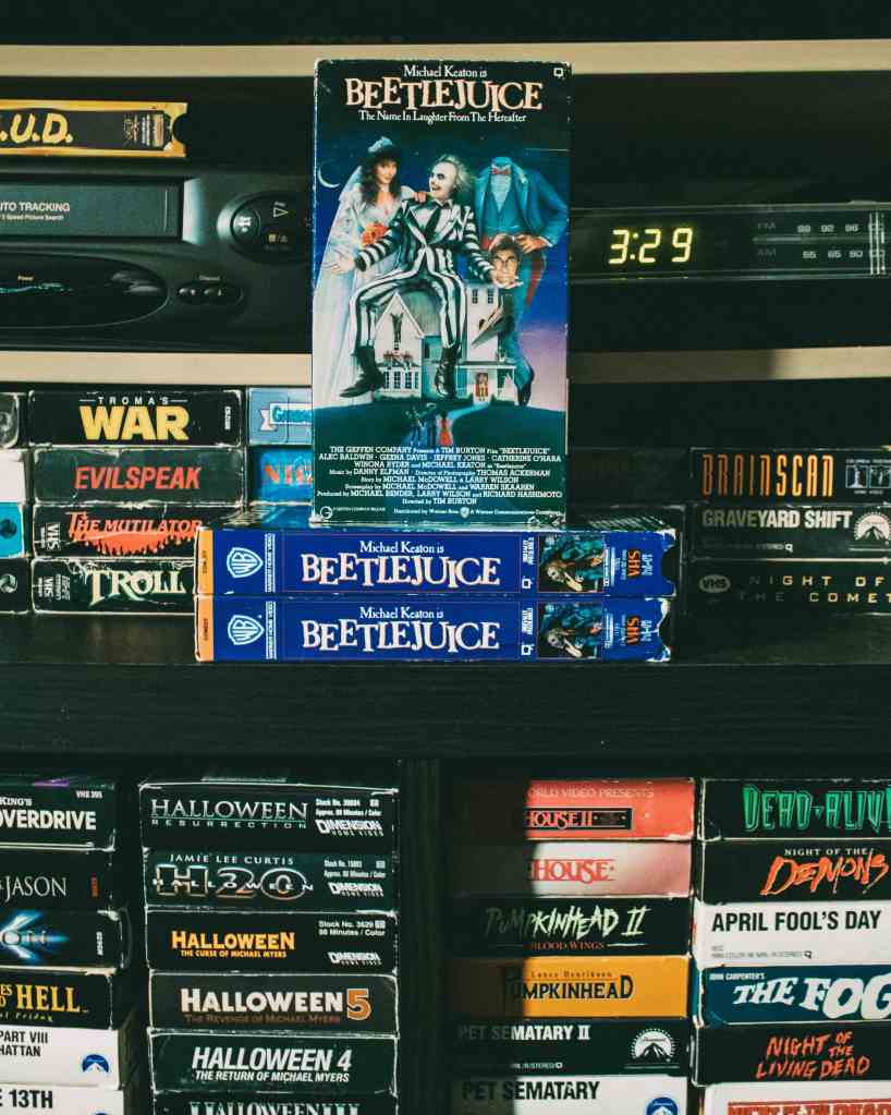 Ein Regal mit VHS-Kassetten, darunter mehrere Kopien von 'Beetlejuice' mit Michael Keaton, sowie andere Horrorfilme der 80er und 90er Jahre.